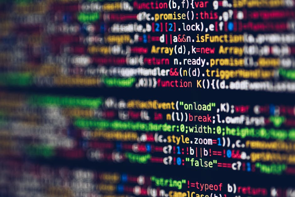 A person working on a MacBook laptop with a dark-themed code editor open on the screen, displaying lines of programming code with highlighted syntax in green, blue, and white. The individual's hands a